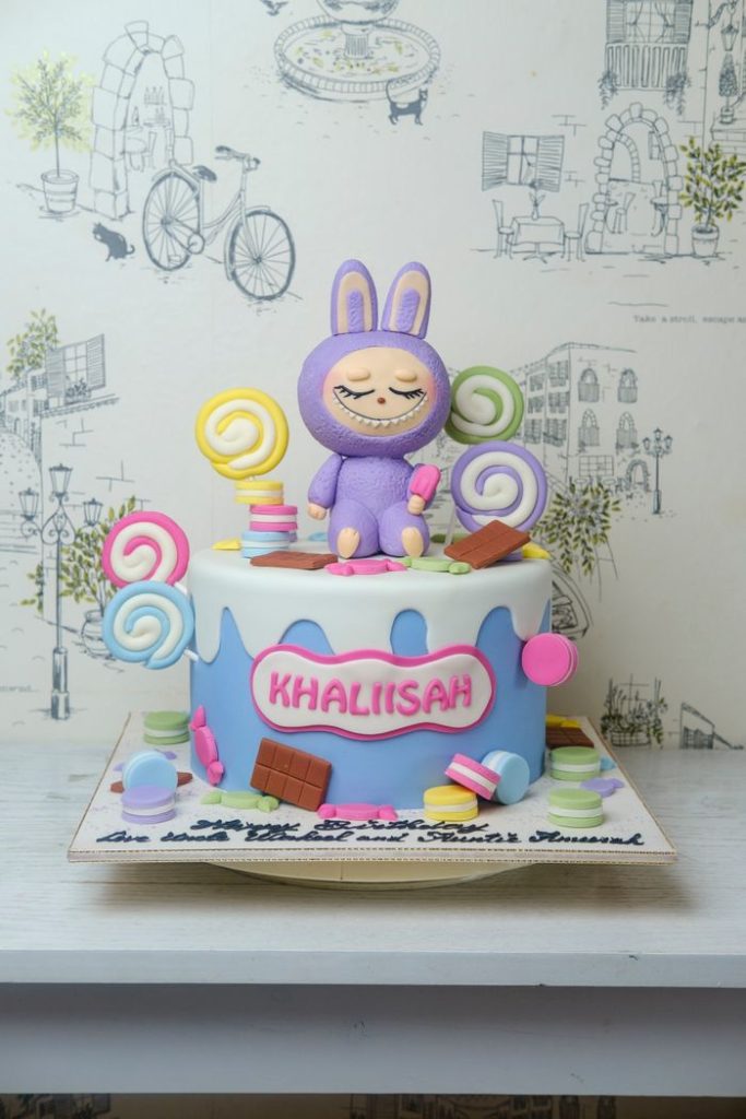 A playful pastel cake with a cartoon character and candies, perfect for children's celebrations.