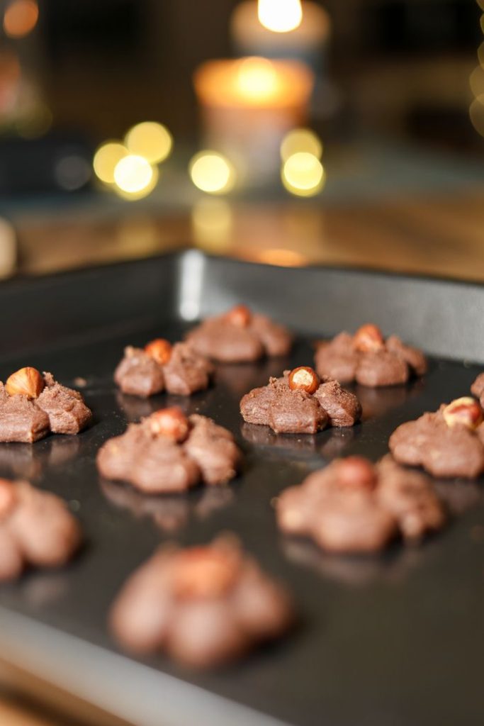 Freshly baked chocolate cookies on a tray, with blurred lights in the background creating a cozy atmosphere.