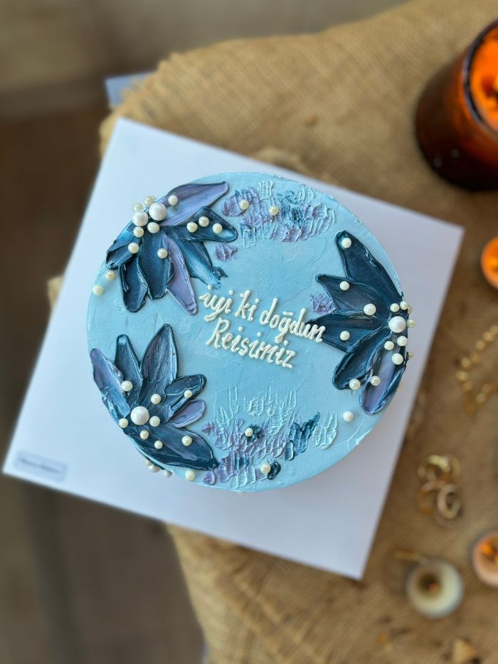 A beautifully decorated blue birthday cake with floral accents and a personal message on top.