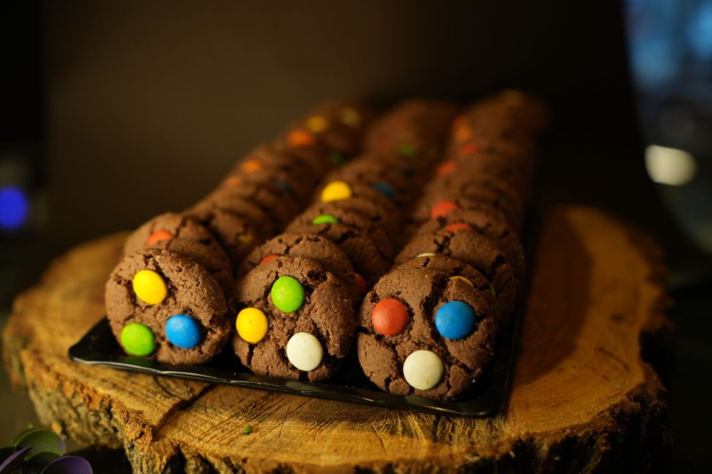 A close-up of vibrant chocolate cookies with colorful candies on a rustic wooden platter.