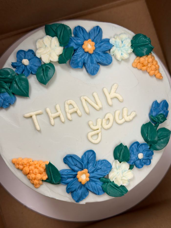 Round cake with 'Thank you' icing and colorful floral decorations.