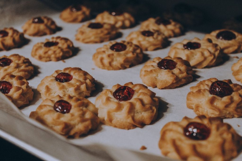 Close-up of homemade cookies topped with cherry jam on a baking sheet.